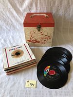 Front view of the vintage carrying case with musical notes printed and handle, lock, records and sleeves displayed alongside