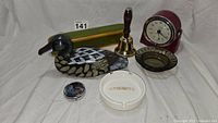 Overview of the lot showing the Kodak alarm clock, carved wood duck, wood pencil box, brass bell, and ashtrays.