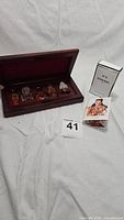 Photo showing the wood case holding five miniature perfume bottles and two boxed perfume items: Chanel No5 and coach sample box, set on white fabric background.