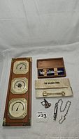 Full lot overview showing weather station, candle snuffer, The Golden Tool, police whistle with chain, and railway-spike bottle opener in box