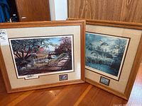 Two framed signed prints, one of a wooden bridge and creek with ducks and another of a wetland with flying birds, both in wood frames.