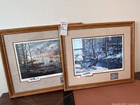 Two framed signed wildlife prints angled side by side showing nature scenes and wooden frames with mats.