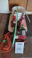 Photo showing battery charger, jack stands, and extension cord strapped together on wooden pallet.