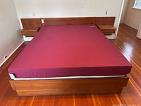 Full view of wooden platform bed with headboard and red-covered mattress