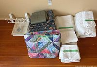 Overview of all bed linens and other fabric items laid out on floor, showing quilts, sheets, pillowcases and folded pieces.