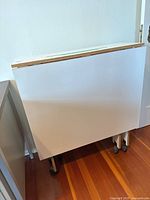 Front view of crafting table folded with both leaves down, showing white panel and caster wheels