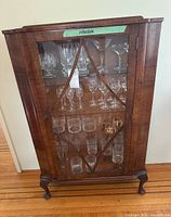 Front view of wooden display cabinet showing glass door with decorative lattice design, glass shelves inside, and key hanging in lock.