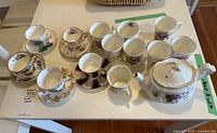 Full photo showing the assorted bone china pieces including teapot, cups, saucers, and mugs arranged on a table
