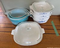 Full set photo showing 1 blue Pyrex mixing bowl and 6 white CorningWare baking dishes stacked and arranged.