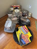 Overview of all kitchen ware and small appliances arranged on the floor, includes blender, coffee grinder, bowls, baking pans, aluminum foil trays, plastic containers, and Glad OvenWare baking set.