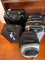 Overview photo showing all five pieces of luggage grouped together on a wooden floor in front of a shelf unit.