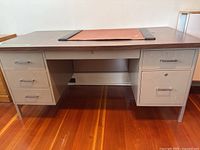 Front view of six drawer beige metal desk with woodgrain top and leather desk pad.