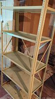 Four-shelf metal shelving unit in corner of basement, beige color, showing rust, dents, and surface grime.