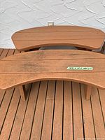 Two outdoor wooden benches side by side showing reddish-brown painted finish, curved slatted seat tops, approximate dimensions labelled on one bench.