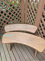 Two brown wooden outdoor benches with curved seats placed on a wooden deck corner.