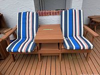 Full view of both chairs connected by center table with cushions in place on wood deck