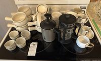 Overview of the entire lot: two French presses, multiple white ceramic soup bowls, ramekins, and coffee mugs arranged on a dark surface.