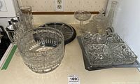 Overview of punch bowl, stemmed glasses, decanter, silver tray, and other glass serve ware on flat surface