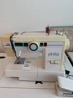 Front-left angle of cream-colored Elnita 220 sewing machine showing stitch selector dial, stitch pattern guide, and foot pedal.