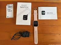 Photo showing smart watch, charger, box and manual laid out on wooden table.