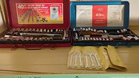 Photo of two 40-piece socket sets in red and blue cases, with a set of five metal open-end wrenches in yellow pouch