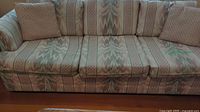 Front view of large three seater sofa with patterned fabric upholstery and three seat cushions.