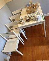 White wooden rectangular kitchen table and four matching chairs arranged on a hardwood floor against a wall, showing the overall set and condition.