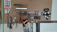 Wide shot of tools arranged on pegboard including locking pliers, saws, axe, measuring tape, pliers, safety glasses, and appliance regulator caps.