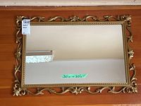 Full view of rectangular wall mirror on wood floor showing mirror glass with 30 x 20 inch measurement note and ornate golden frame.