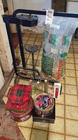 Photo showing a floor standing wine press, glass bottles, metal tins with decorative lids, large bags of wine corks, and a temperature measuring device.
