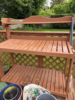 Front view of brown wooden patio workbench or plant stand showing two slatted shelves and lattice woodwork back panel.