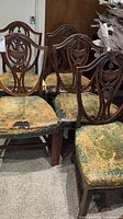 Five antique wooden dining chairs grouped together showing carved backs and damaged upholstery.