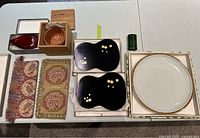 Lot items displayed on table, showing placemats, black lacquered trays, pottery bowl, red glass dish, decorative trivets, and round serving plate.