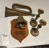 Photo showing the full lot including brass horn, wall-mounted bell on plaque, and two brass candlesticks on a white surface.