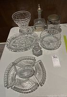 Photo of crystal serveware collection including decanter, covered jar, pedestal bowl, round bowl, and divided serving dish placed on a white surface.