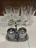 Front view of eight crystal stem glasses and glass/metal condiment set on a white surface.