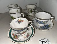 Photo showing five fine china teacups with matching saucers, each featuring different floral designs and gold accents.