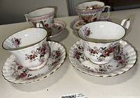 Photo showing four fine china teacups with matching saucers, floral rose pattern and gold edge trim.
