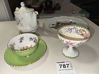 Assorted fine bone china items including a teapot, multiple cups with floral patterns, saucers, and a small serving plate.