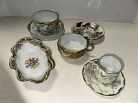 Full assortment of fine china items with gold accents visible under bright light on white surface.