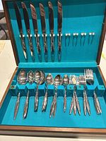 Full view of open wooden case showing knives, forks, spoons, and butter knives neatly organized in blue velvet slots.