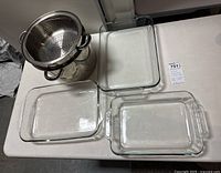 Overhead image showing two clear rectangular glass casserole dishes with handles and a stainless steel metal pot with two strainers inside, placed on a table.