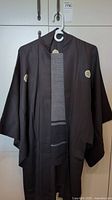 Front view of the dark brown kimono with white embroidered crests visible on the sleeves and chest area.
