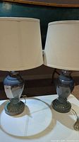 Pair of ceramic blue base table lamps with white shades on top of a table, showing overall condition and size.