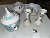 Photo showing six ceramic pieces: a teapot with blue bird pattern, a lidded bowl with floral motif, a round dish with birds, and two white ceramic candleholders with floral designs.