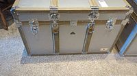 Front view of vintage metal trunk showcasing central lock, three silver-tone latches, and olive green metal reinforcements with rivets.