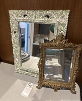 Large carved wood frame mirror and smaller brass frame mirror shown together on a surface
