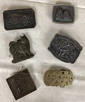 Top view of six vintage belt buckles arranged on a flat surface, showing design details and varying shapes including a dog figure and logos.