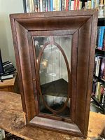 Photo showing front view of antique wooden hanging corner cabinet with glass door and oval decorative frame