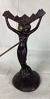 Front view of the metal nude female figure lamp showing the pose and winged fan above the head.